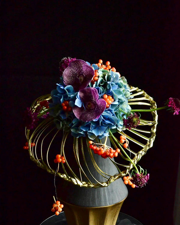 Intermediate floristry course, student holding a collar bouquet with hydrangeas, vanda, viburnum berries and scabiosa, featuring bear grass braiding technique