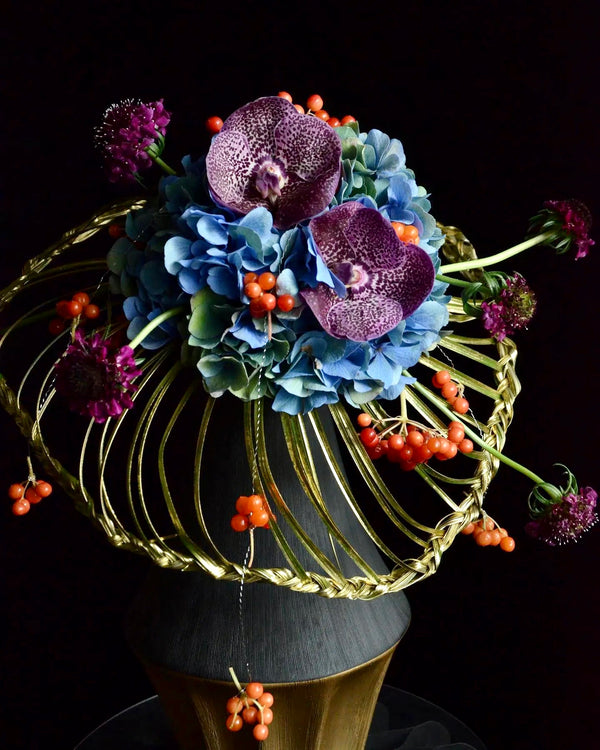 Intermediate floristry course, student holding a collar bouquet with hydrangeas, vanda, viburnum berries and scabiosa, featuring bear grass braiding technique