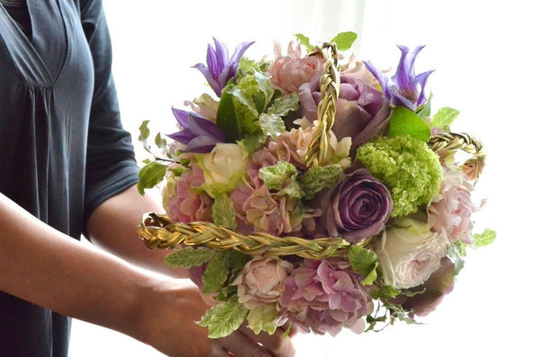 Intermediate floristry course, student holding a bouquet in bouquet holder with hydrangeas, roses, viburnum and clematis, featuring bear grass braiding technique