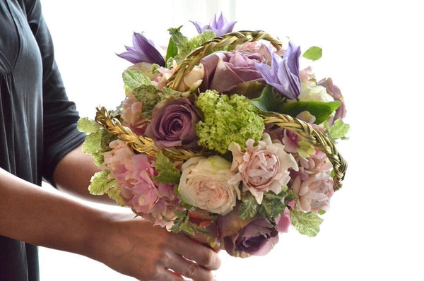 Intermediate floristry course, student holding a bouquet in bouquet holder with hydrangeas, roses, viburnum and clematis, featuring bear grass braiding technique