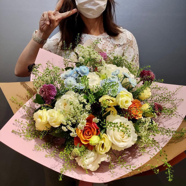 Intermediate floristry course, student holding a hand tied bouquet with roses, lisianthus, scabiosa, spray chrysanthemums, ammi majus and thlaspi