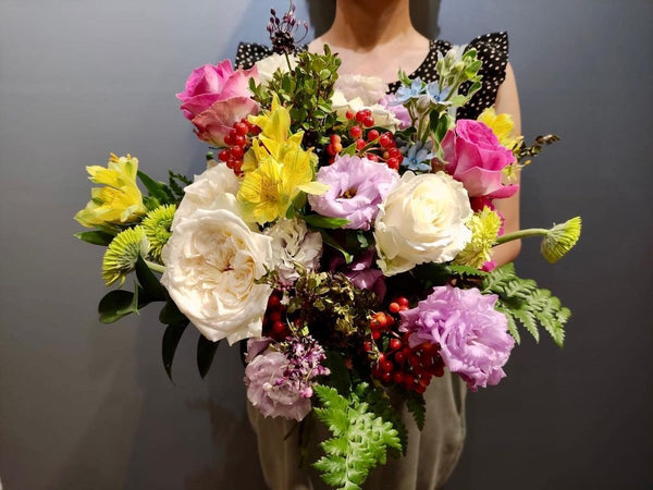 Intermediate floristry course, student holding a hand tied bouquet with roses, lisianthus, alstroemeria, viburnum berries, oxypetalum and asters