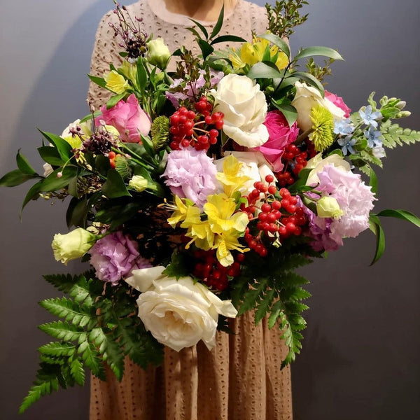 Intermediate floristry course, student holding a hand tied bouquet with roses, lisianthus, alstroemeria, viburnum berries, oxypetalum and asters