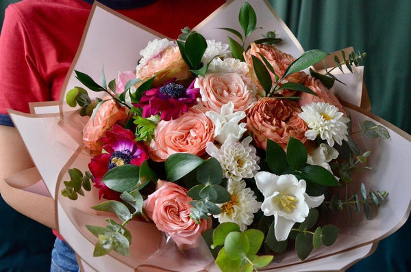 Intermediate floristry course, student holding a hand tied bouquet with roses, dahlias, tulips, and anemone