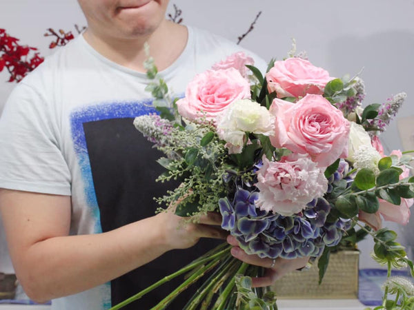 Hand-tied Bouquet Workshop, student making a hand tied bouquet with hydrangeas, roses, mentha, lisianthus and acacia