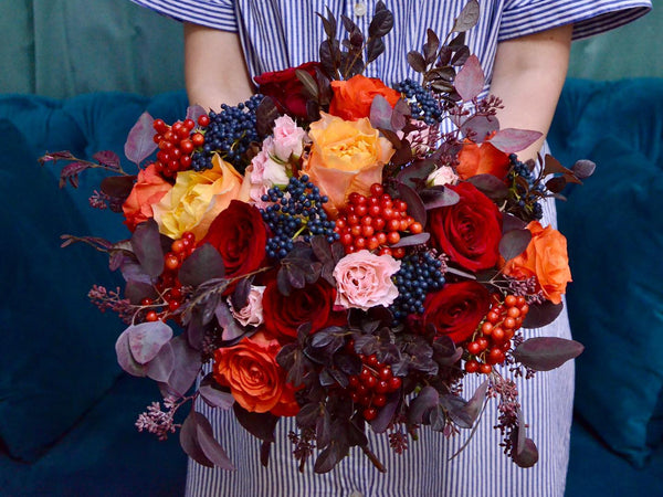 one day taster workshop, student holding a finished hand tied bouquet in autumnal colours with roses, viburnum berries and dyed seeded eucalyptus
