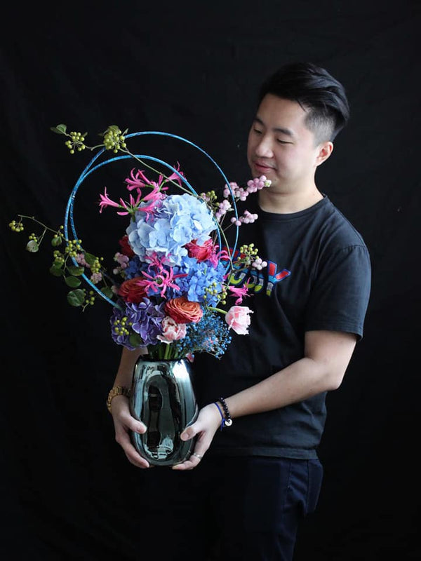 one day taster workshop, student holding a finished vase arrangement with hydrangeas, roses, nerine, tulips,  gypsophila and symphoricarpos