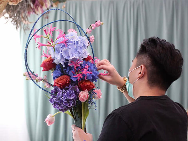 Hand-tied Bouquet Workshop, student making a hand tied arrangement with hydrangeas, roses, tulips, nerine, gypsophila and symphoricarpos