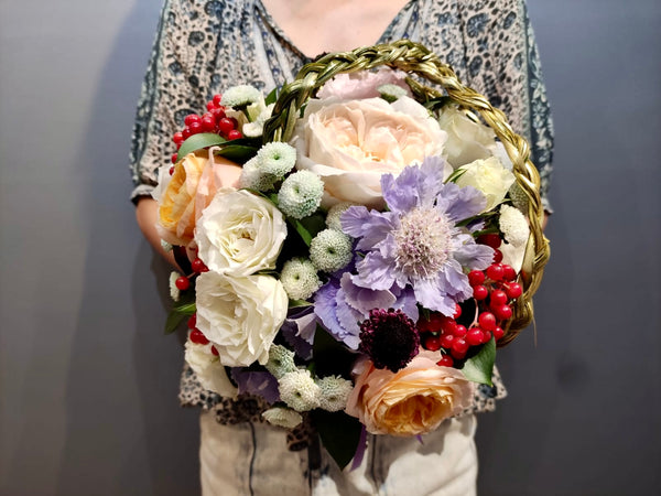 Intermediate floristry course, student holding a bouquet in bouquet holder with hydrangeas, roses, viburnum berries and scabiosa, featuring bear grass braiding technique