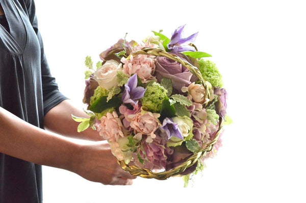 Intermediate floristry course, student holding a bouquet in bouquet holder with hydrangeas, roses, viburnum and clematis, featuring bear grass braiding technique