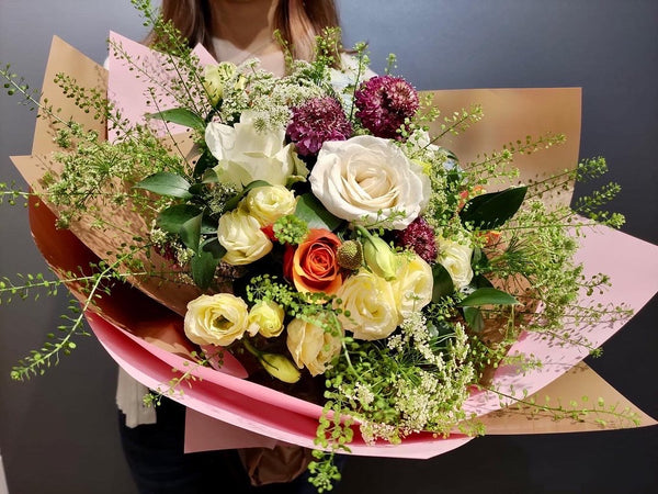 Intermediate floristry course, student holding a hand tied bouquet with roses, lisianthus, scabiosa, spray chrysanthemums, ammi majus and thlaspi