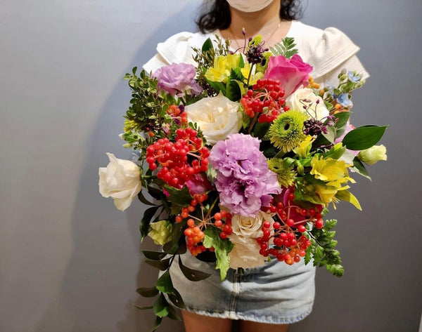 Intermediate floristry course, student holding a hand tied bouquet with roses, lisianthus, alstroemeria, viburnum berries, oxypetalum and asters